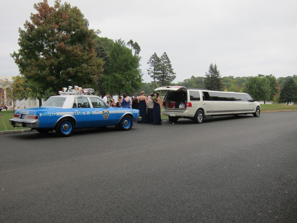 police car and white limousine parked side-by-side with people standing around