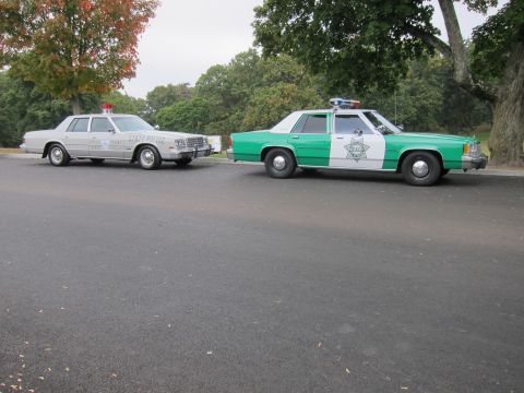 2001 Ford Crown Victoria - Two police cars are parked side-by-side on a paved surface, with trees in the background.