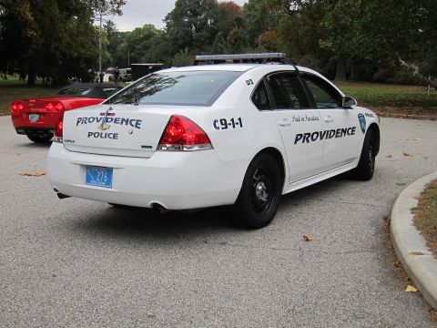 2001 Ford Crown Victoria - A white police car with Providence markings is parked on asphalt, with a red sports car in the background.