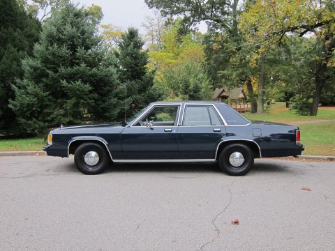 2001 Ford Crown Victoria - A dark blue sedan with chrome accents is parked on a street with trees and a small building in the background.