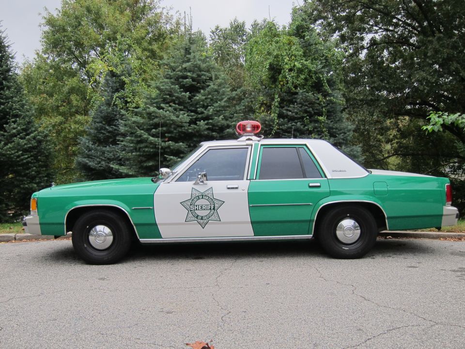 Side view of a green and white Sheriff's car, likely a Ford LTD or similar from the 1980s