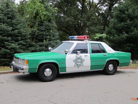 2001 Ford Crown Victoria - This sheriff's car, likely from the 1980s, features a distinctive green and white paint scheme and a light bar on the roof.
