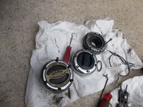 1995 Ford Bronco - Two Warn locking hubs are laid out on a white paper towel on a concrete surface. Tools including a screwdriver and pliers are also visible.