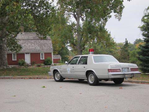2001 Ford Crown Victoria - A Rhode Island State Police car with a light bar on top is parked on a paved surface.