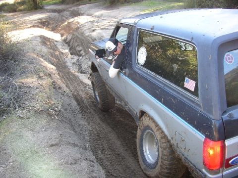 1989 Ford Bronco - A person leans out the window of a Ford Bronco as it navigates a muddy, rutted trail.