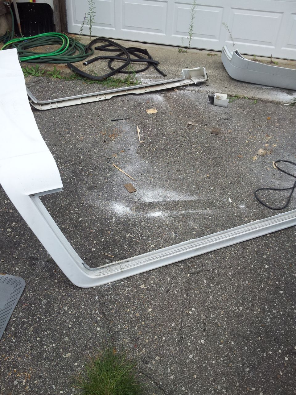 Car door trim piece and a bumper section lying on asphalt in front of a garage door