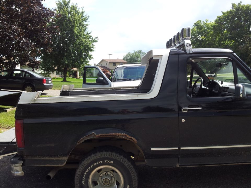Black Ford Bronco with chrome trim and light bar on roof, parked next to a silver pickup truck