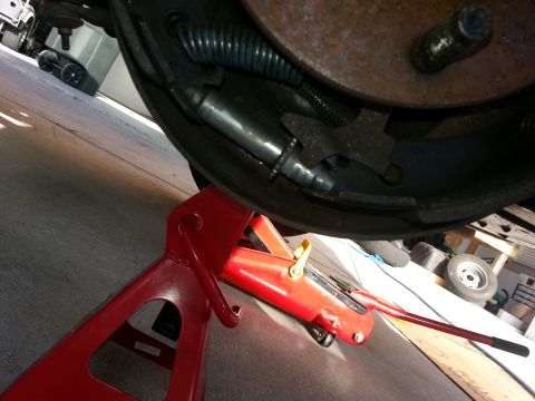 1994 Ford Bronco - Photograph of a rear drum brake and brake line with a red floor jack positioned under the vehicle.