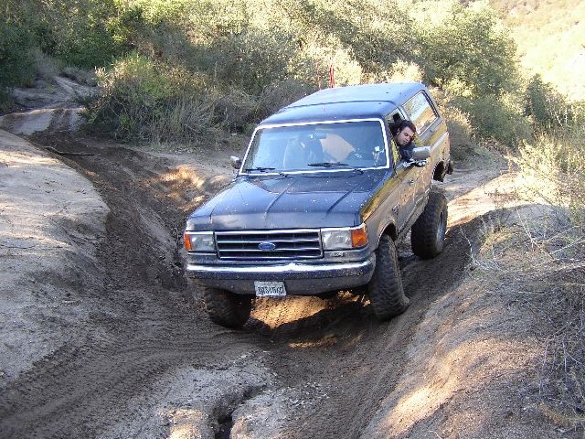Dark Ford Bronco SUV on rutted dirt off-road trail, front 3/4 view