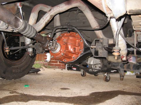 1994 Ford Bronco - The underside of a vehicle shows the rear differential housing painted bright orange, connected to the driveshaft. The suspension component…