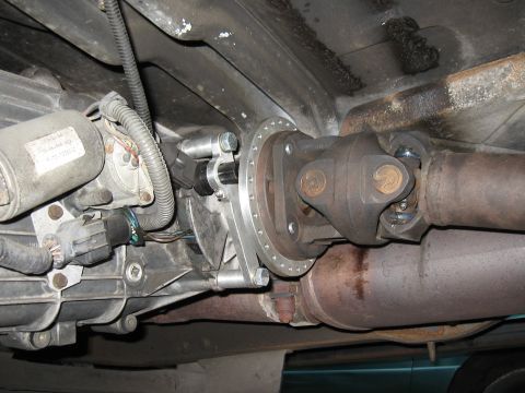1994 Ford Bronco - Underneath view of a vehicle's drivetrain showing a transfer case, driveshaft, and part of the exhaust system. A silver adapter plate is bo…