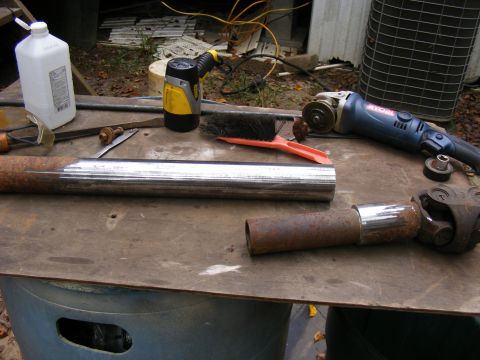 Metal driveshaft on a workbench with a grinder and cleaning bottle.