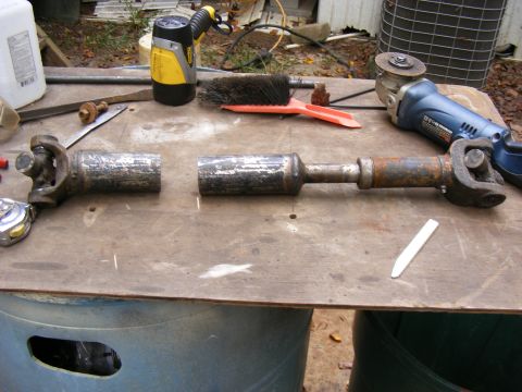 Two driveshaft pieces on a workbench with tools.