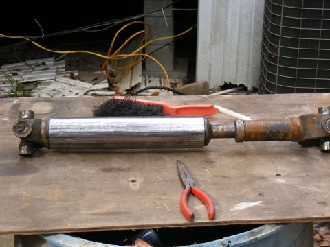 Driveshaft with U-joints and center support on a wooden surface with pliers and brush
