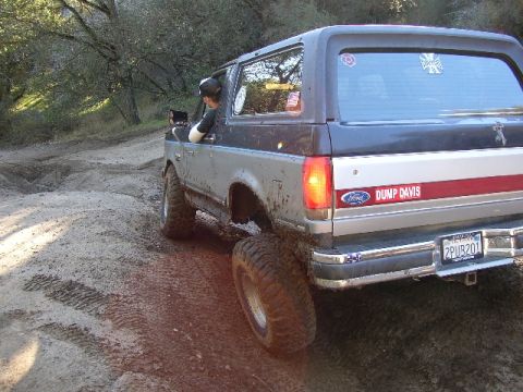 1989 Ford Bronco - 1989 Ford Bronco navigates a muddy off-road trail with its brake lights illuminated.