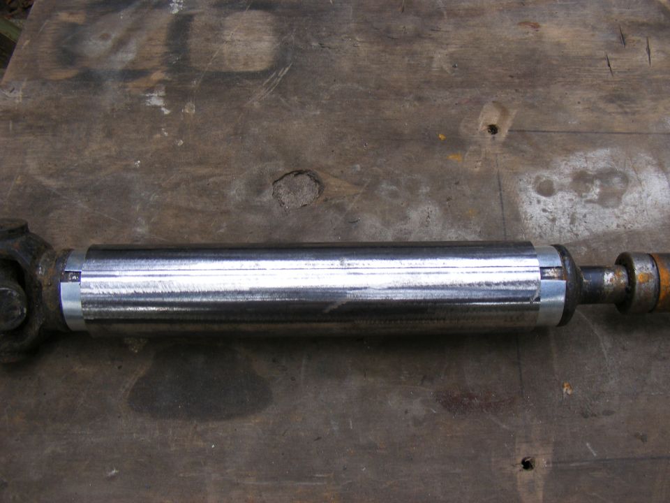 Driveshaft with polished metal tube on a wooden surface.