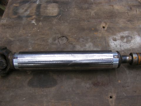 Shiny metal driveshaft with U-joints on a wooden surface.