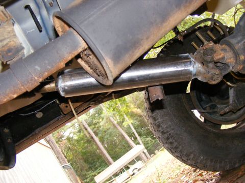 Underside of a vehicle showing a new chrome exhaust pipe extension and part of the rear axle and tire.