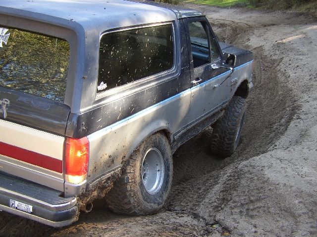 Two-tone gray Ford Bronco SUV on muddy rutted off-road trail, rear 3/4 view