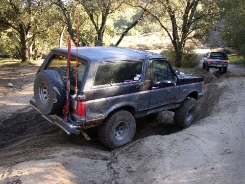1989 Ford Bronco - A black Ford Bronco navigates a dirt path with another SUV in the background.
