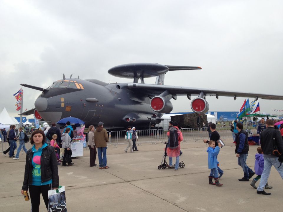 Large gray aircraft with radar dome on top, people walking around.