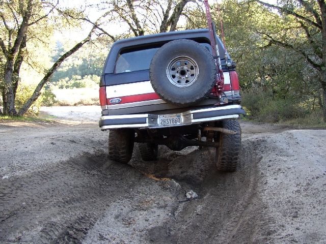 Rear of red/white Ford Bronco on rutted off-road dirt trail