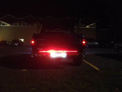 1996 Ford Bronco - The rear of a dark-colored SUV, likely a 1996 Ford Bronco, is visible at night. The brake lights are illuminated, with an additional light…