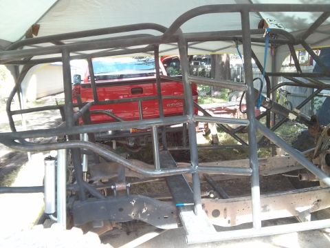 1986 Ford Bronco - A custom roll cage is being constructed around the chassis of a red Chevrolet pickup truck, which is partially visible under a white canopy…