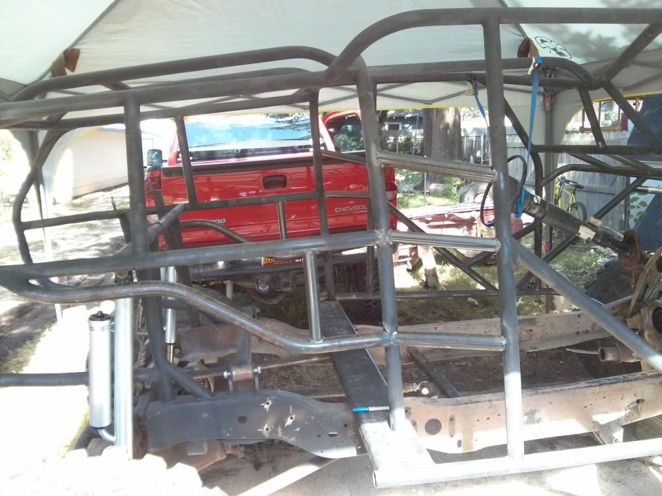 Custom roll cage construction around a red Chevrolet pickup truck chassis.