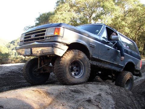 1989 Ford Bronco - This Ford Bronco is navigating a steep, muddy incline with its driver's side door ajar.