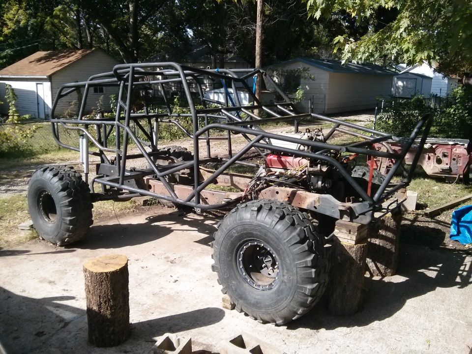 Custom off-road buggy with roll cage and large tires, in progress, outdoors.