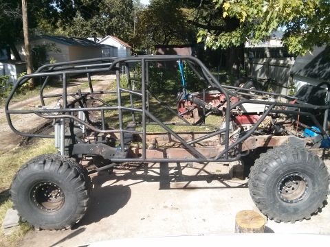 1986 Ford Bronco - A custom-built off-road buggy with a roll cage is shown in a yard with trees and houses in the background. The vehicle has large, aggressiv…