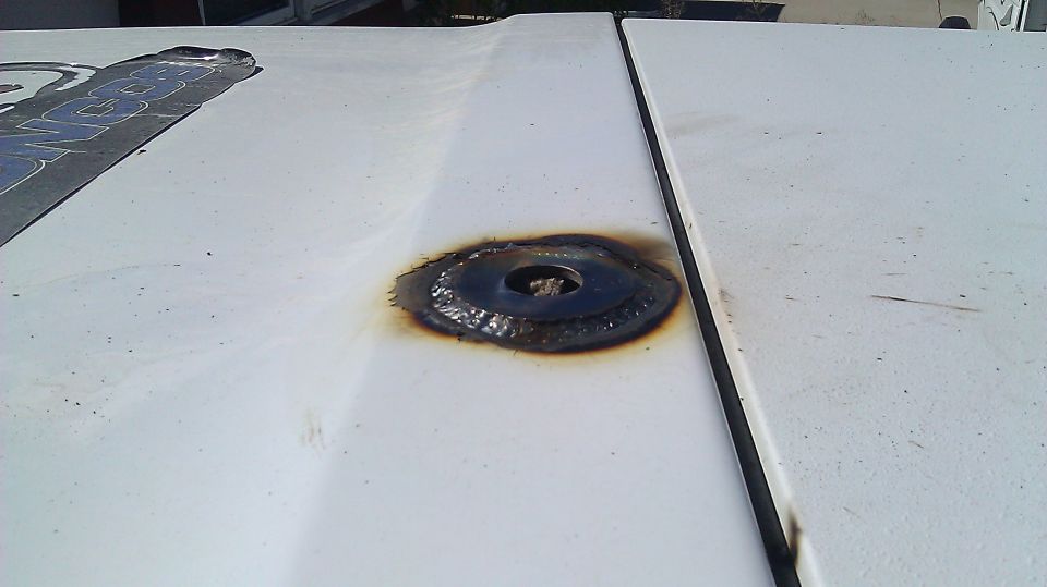 Welded metal plate on white vehicle hood with partial decal