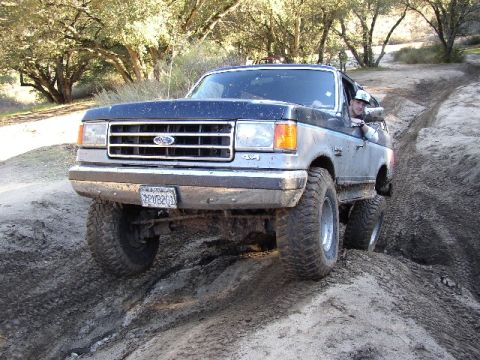 1989 Ford Bronco - A Ford Bronco navigates a muddy off-road trail with a driver visible inside.