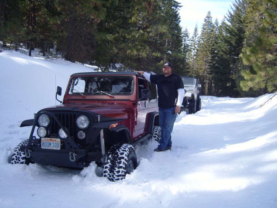 Man standing next to a red Jeep CJ7 in the snow.