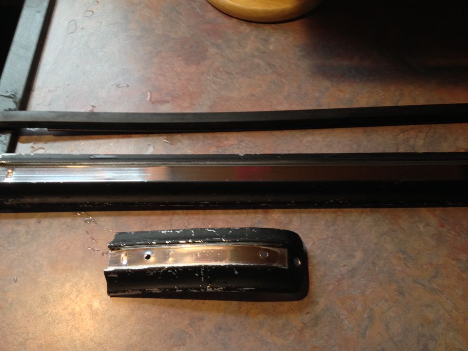 Three pieces of black rubber trim with metal accents on a textured surface.