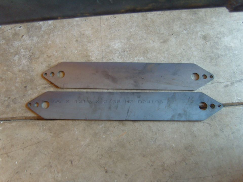 Two metal plates with holes on concrete, one with etched text.