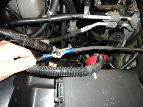 2004 Mercury Grand Marquis - A hand is shown connecting a black wire with a blue connector to a terminal on a vehicle's battery system. The wire is routed through black…