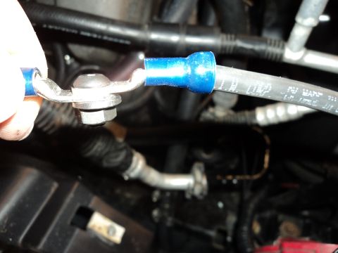 2004 Mercury Grand Marquis - A close-up view shows a hand holding a metal lug connected to a blue insulated wire, which is secured by a bolt and nut. The lug is attache…