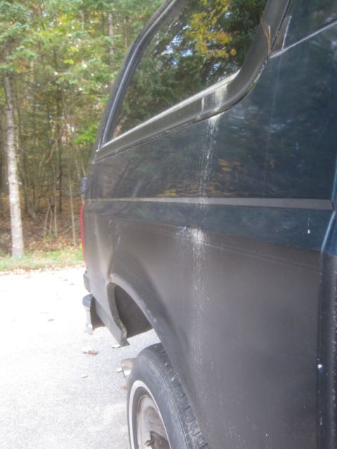 1993 Ford Bronco - A close-up, high-angle shot of the rear quarter panel and wheel well of a dark-colored SUV, showing some scuff marks and scratches on the b…