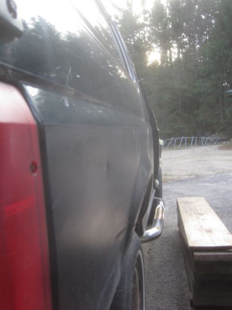 1993 Ford Bronco - Low angle view of the lower rear quarter panel and exhaust tip of a dark colored vehicle, possibly a Ford Bronco, with a red taillight visi…
