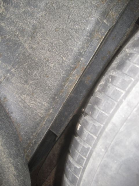 1993 Ford Bronco - Close-up view of the inner fender well of a vehicle, showing the tire and part of the undercarriage. The metal shows signs of rust and dirt…