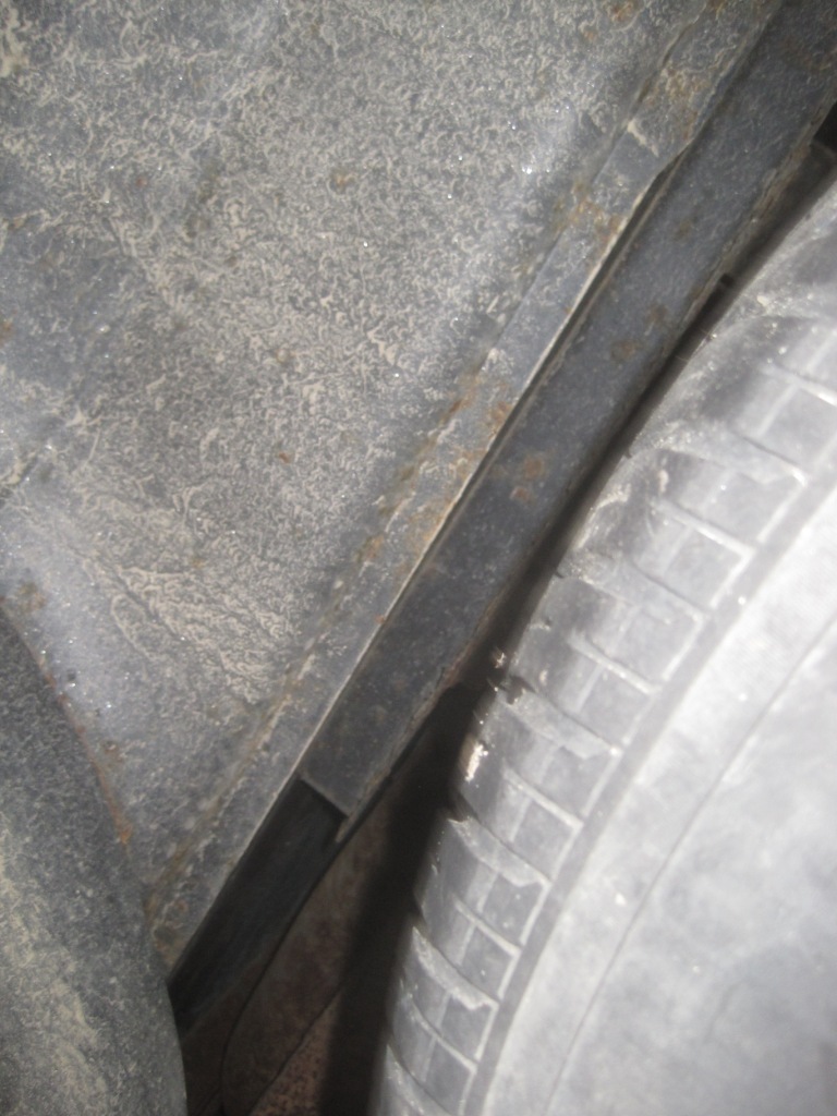 Close-up of a vehicle's inner fender well with tire and rusty metal.