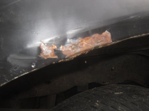 1993 Ford Bronco - Close-up view of rust damage on the lower body panel of a vehicle, with the tire and undercarriage visible below.