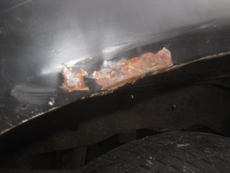 Close-up of rust on a vehicle's lower body panel near the wheel well.