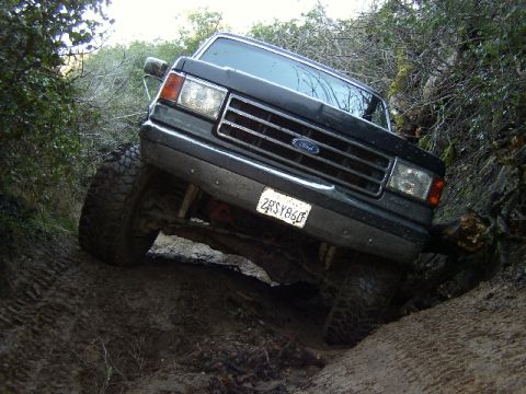 1989 Ford Bronco - This Ford Bronco is navigating a challenging, muddy off-road path with steep inclines.