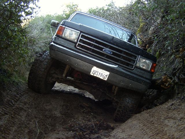 Dark Ford SUV flexing over rutted dirt trail on off-road tires, front view.