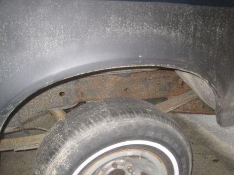 1993 Ford Bronco - A close-up view of the rear wheel well of a vehicle, showing significant rust on the frame and suspension components. The tire is visible w…