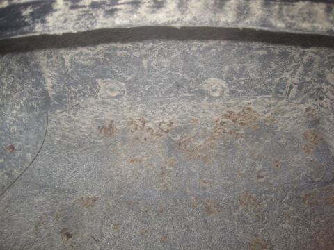 1993 Ford Bronco - A close-up view of the underside of a vehicle, showing areas of rust and dirt accumulation on a dark gray surface. Two circular fasteners a…