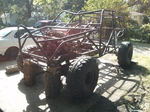 1986 Ford Bronco - A custom-built off-road buggy frame with a V8 engine is shown supported by logs and cinder blocks. A white sedan and a red pickup truck are…